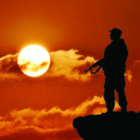 Silhouette of military soldier or officer with weapons at sunset. shot, holding gun, colorful sky, mountain, background